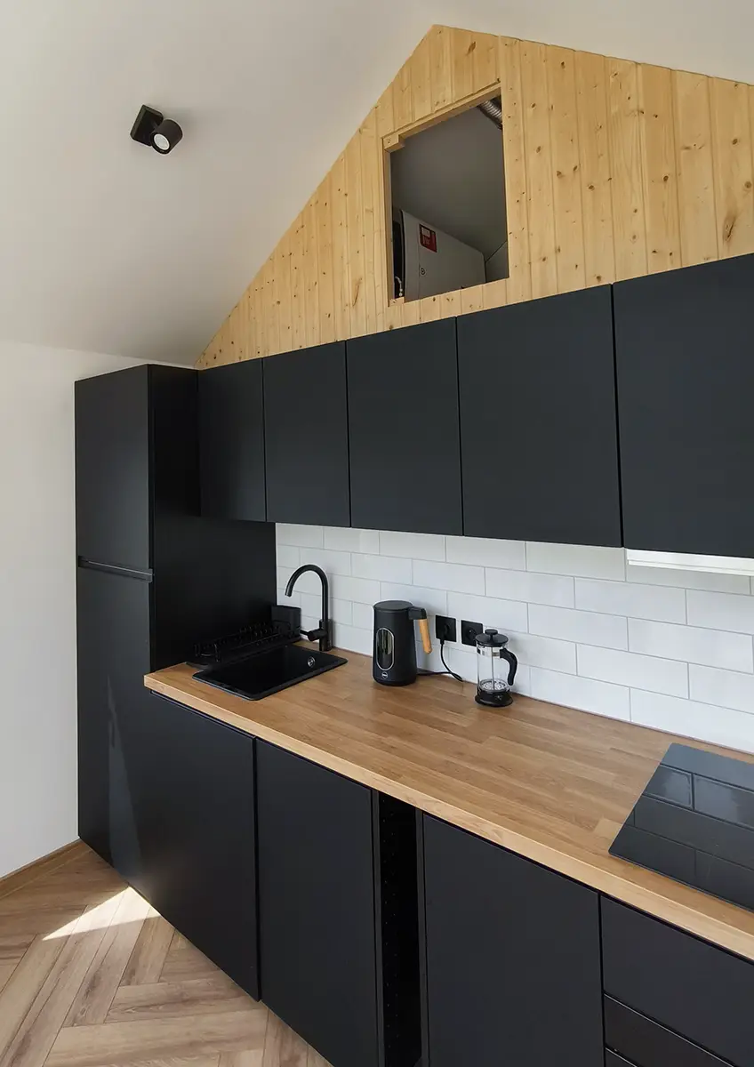 Nowoczesna kuchnia w domu modułowym klienta for.rest house z czarną zabudową i drewnianym blatem.