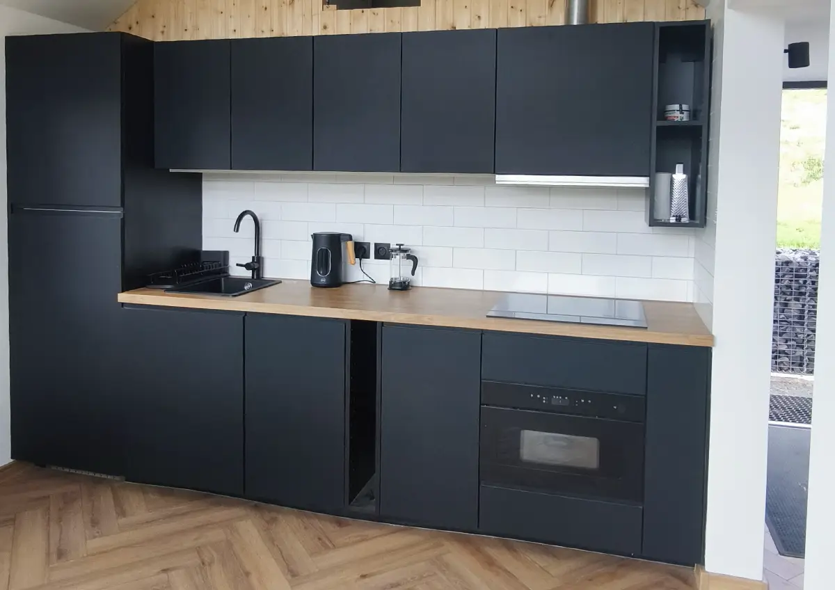 Nowoczesna kuchnia w domu modułowym klienta for.rest house z czarną zabudową i drewnianym blatem.
